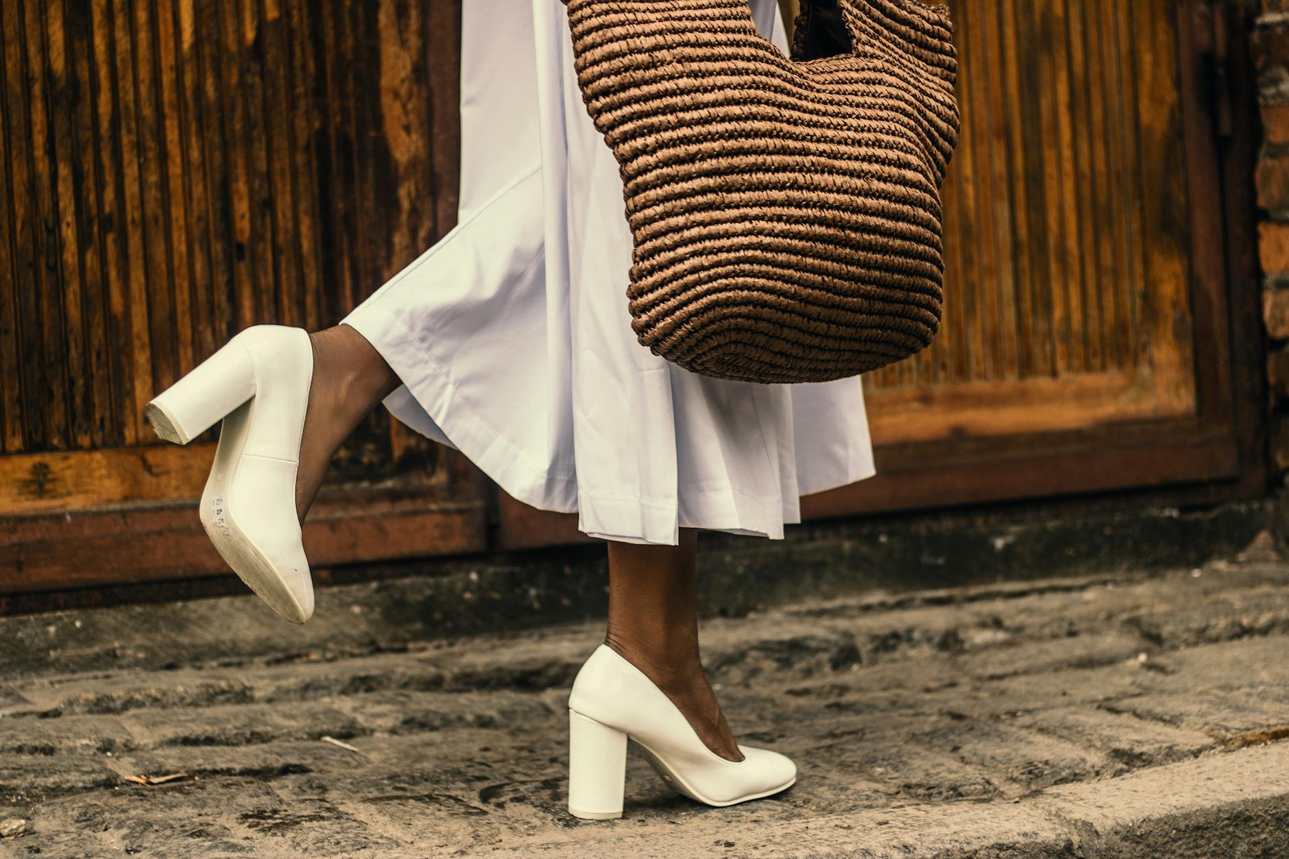 woman wearing white dress and white high heeled shoes while walking on sidewalk
